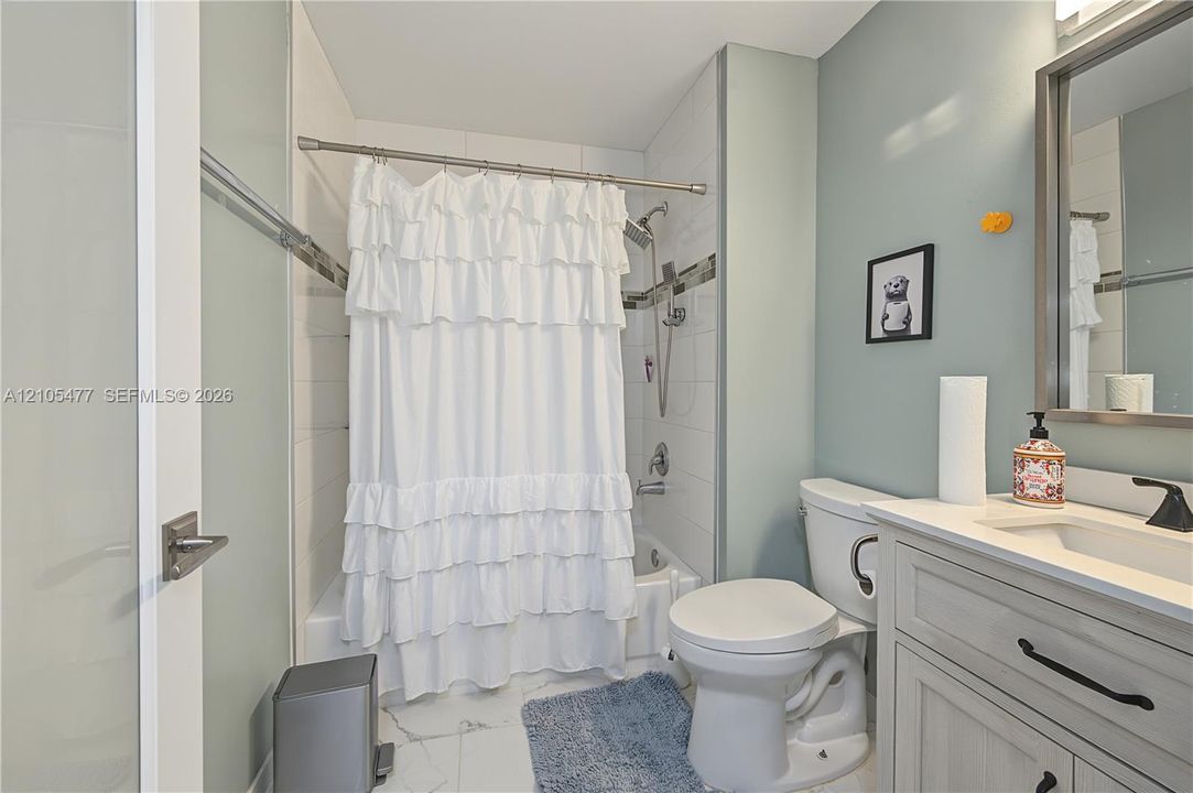 White subway tile shower surround with a metal accent band, white bathtub, single vanity with a white countertop and integrated sink, matte black faucet, and a wall-mounted mirror