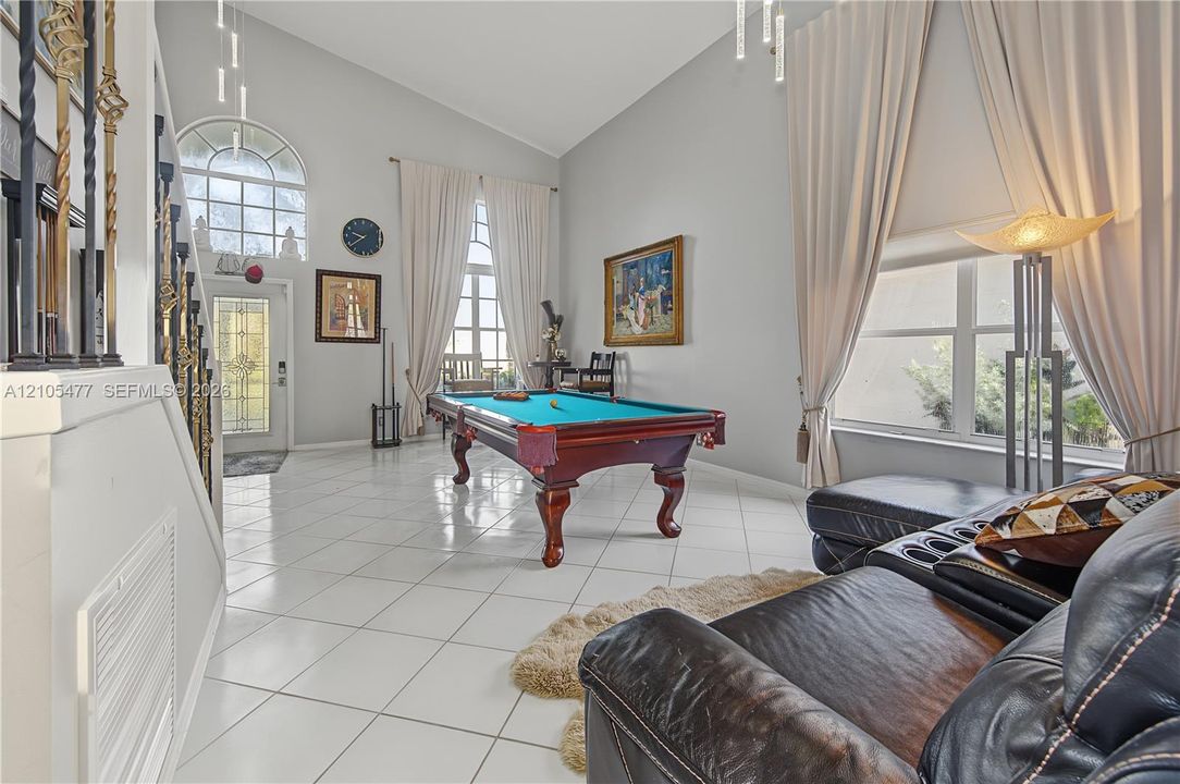Vaulted ceiling, arched transom window, tiled flooring, decorative wrought iron stair railing, and tall windows with drapes