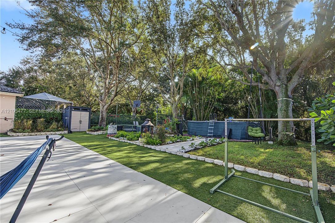 Expansive backyard featuring artificial turf, mature trees, a concrete patio, and a built-in garden bed