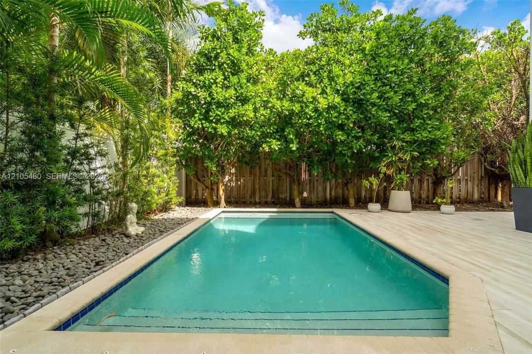 Private swimming pool with integrated steps, surrounded by light-toned decking, a stone perimeter, and lush tropical landscaping