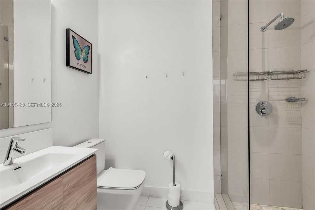 Bathroom featuring a floating wood-finish vanity, integrated rectangular sink, wall-mounted mirror, and a glass-enclosed shower with a rainfall showerhead