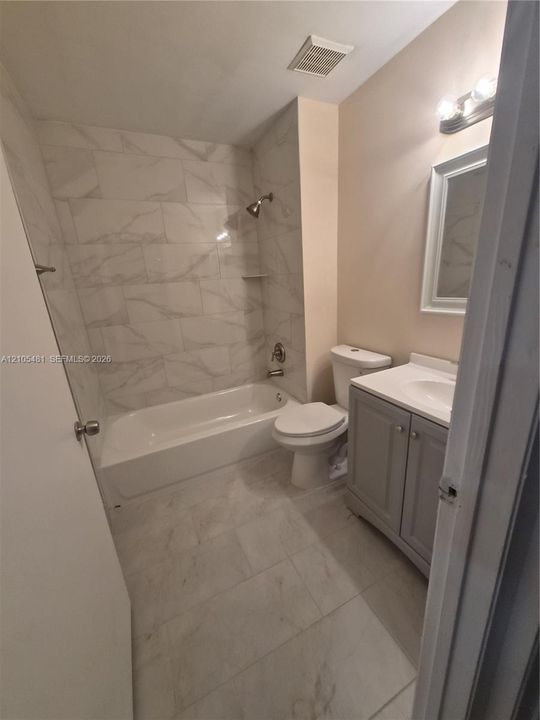 White tile flooring, white tile tub surround, white bathtub, vanity with a white sink, and a rectangular mirror