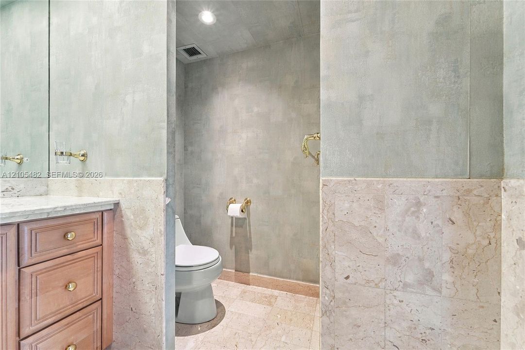 Custom wood vanity with stone countertop, large-format mirror, brass-finish fixtures, and full-height stone tile wainscoting