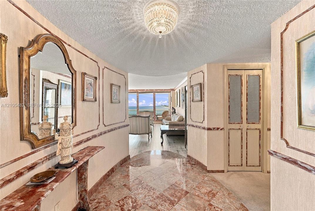 Foyer featuring polished stone tile flooring, decorative wall molding, a tiered crystal ceiling fixture, and a built-in stone console