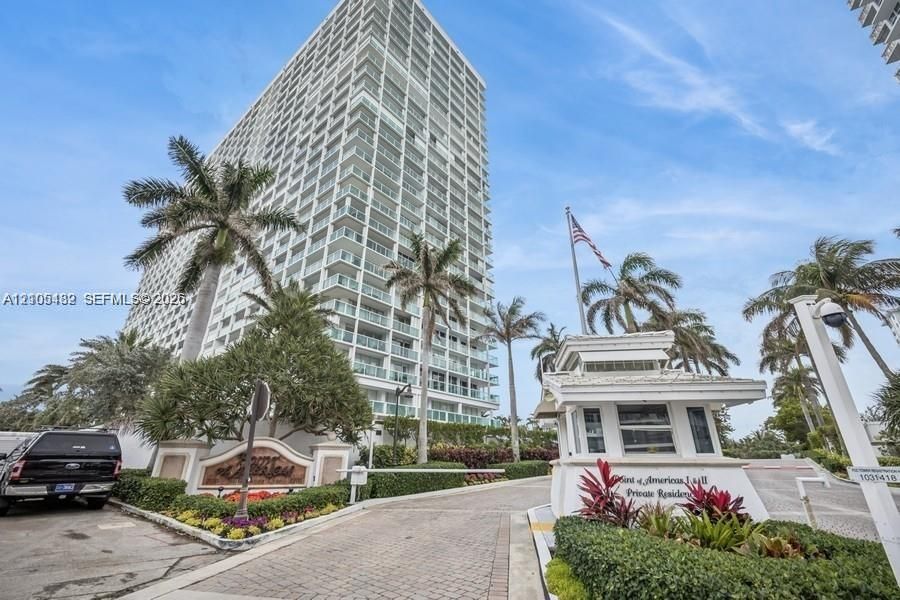 High-rise residential exterior featuring a gated entry with a dedicated security kiosk, paver driveway, and professional landscaping with mature palm trees