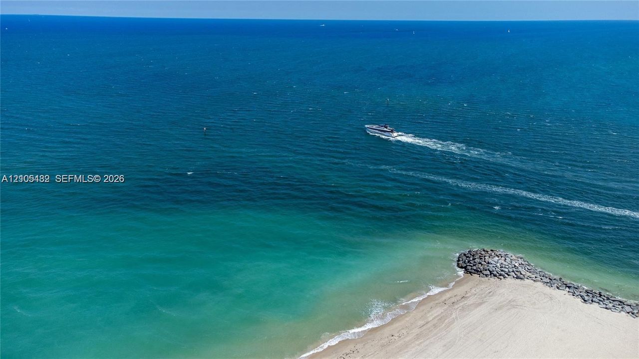 Coastal property featuring direct water frontage, a sandy beach, and stone-reinforced shoreline