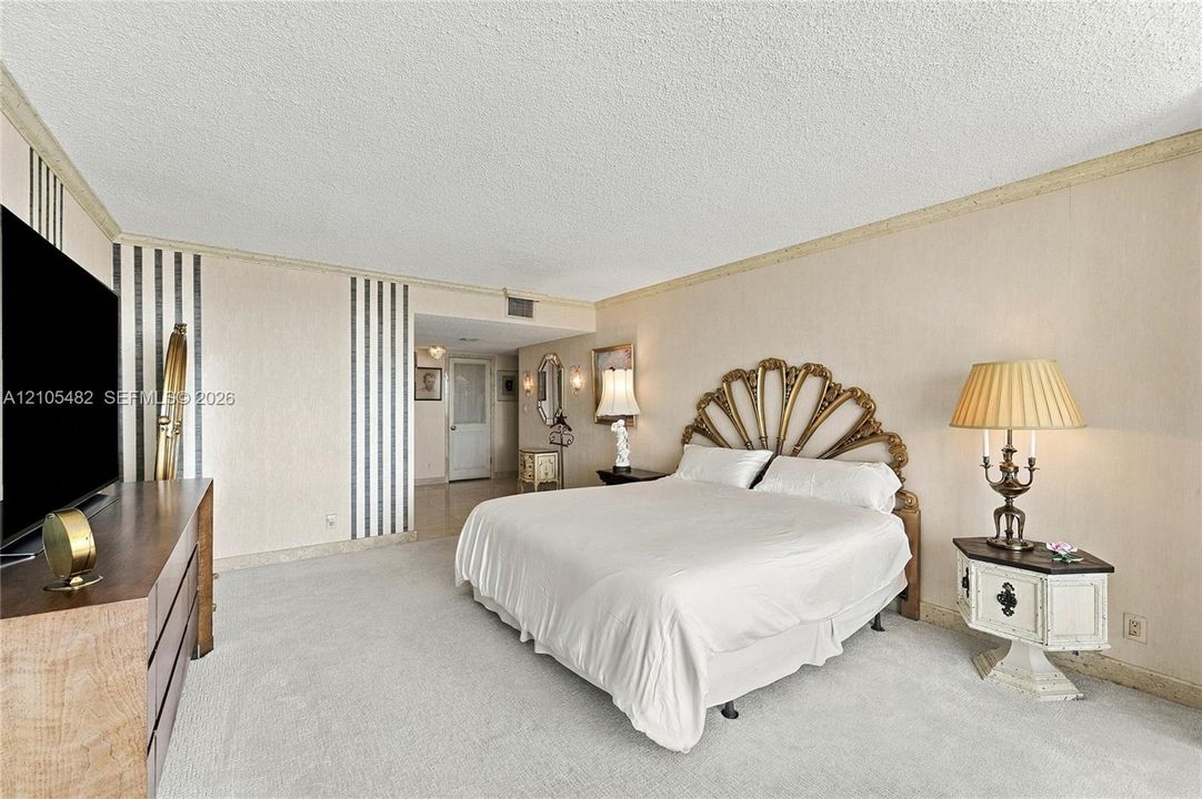 Spacious room featuring vertical striped wall treatments, neutral carpeting, textured ceiling, and crown molding