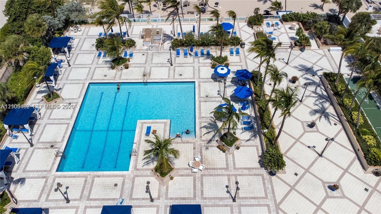 Swimming pool with multi-lane configuration, expansive stone-paver sun deck, integrated tropical landscaping, and surrounding pedestrian pathways
