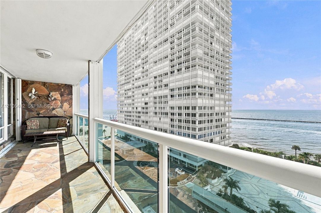 Private balcony featuring natural stone flooring, a decorative stone accent wall, and glass panel railing with a metal handrail