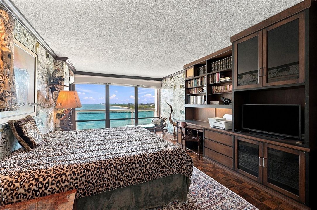 Floor-to-ceiling windows with water backdrop, built-in dark wood cabinetry with integrated shelving and desk, and parquet wood flooring