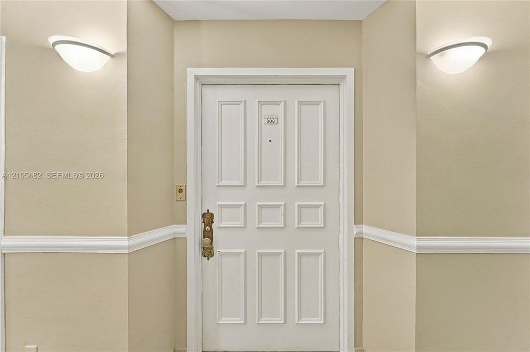 White six-panel entry door with metallic hardware, dual wall-mounted semi-flush mount fixtures, and chair rail molding