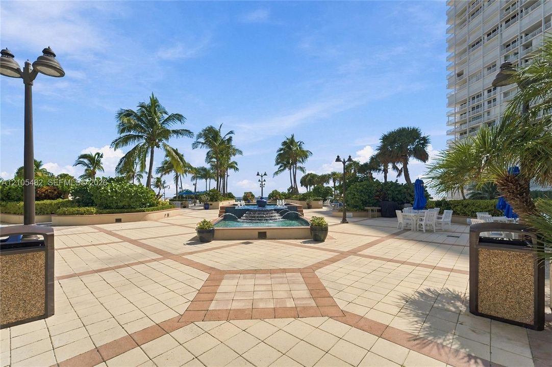 Terrace featuring paver hardscaping, a multi-tiered stone fountain, mature palm trees, decorative post lighting, and built-in landscape planters