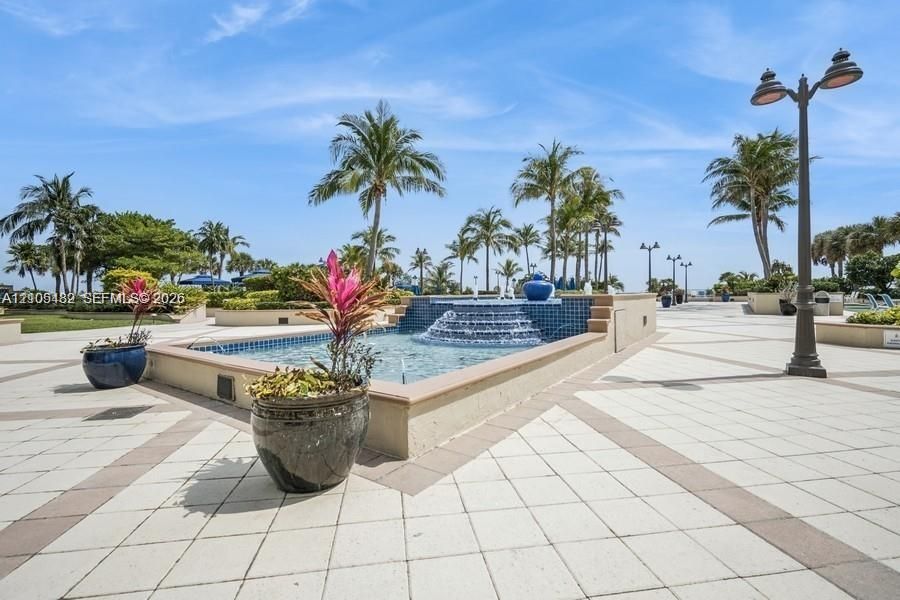 Exterior courtyard featuring a tiered fountain with blue decorative tile, paved walkways, and mature palm trees