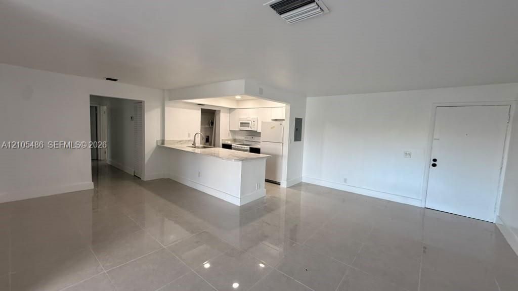 Open-concept living space featuring high-gloss tile flooring, stone-finish breakfast bar, and white cabinetry