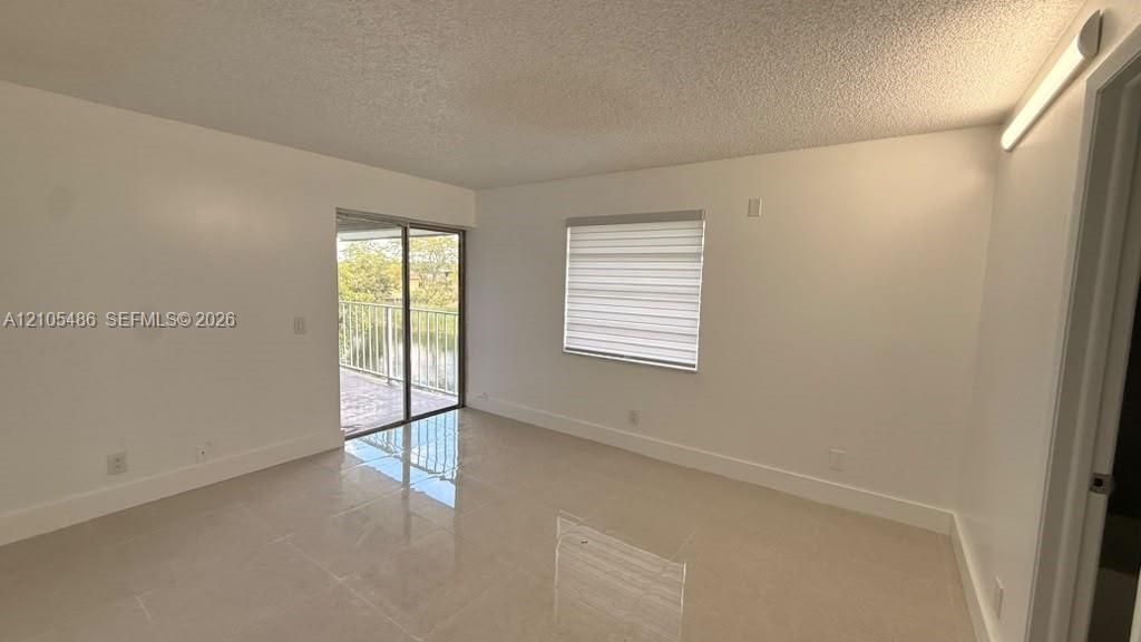 Neutral-toned tile flooring, sliding glass door with access to a railed balcony, and adjustable window treatments