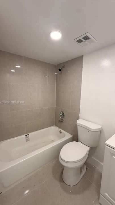 Bathroom featuring a neutral tile surround in the tub area, porcelain-finish tub, chrome-finish shower hardware, and high-gloss tile flooring