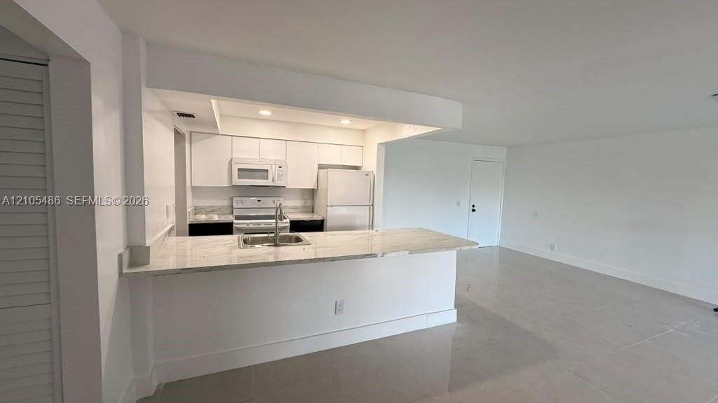 Kitchen featuring stone-patterned countertops, white cabinetry, integrated appliances, and a breakfast bar with an undermount sink