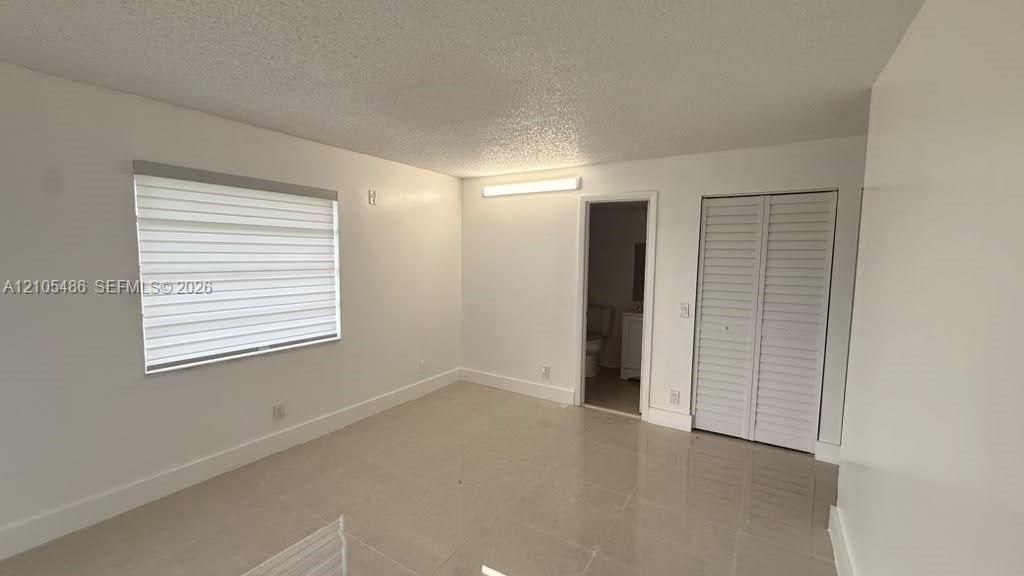 Interior space featuring neutral tile flooring, louvered bi-fold closet doors, and adjustable horizontal window shades