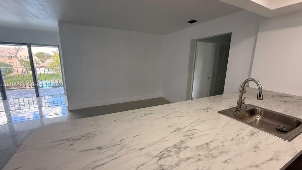 Kitchen island featuring a stone-finish countertop, undermount stainless steel sink, and high-arch faucet, complemented by polished floor tiles and sliding glass door access to a balcony
