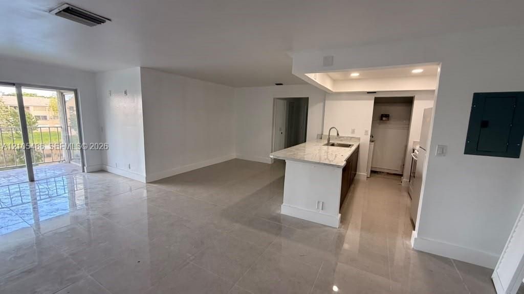 Open-concept interior featuring large-format tile flooring, a kitchen island with stone-finish countertops, recessed lighting, and sliding glass doors