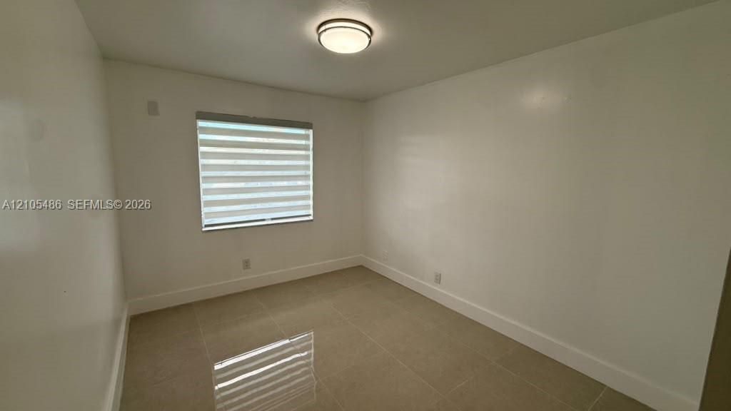 Room featuring neutral-toned tile flooring, light-colored walls, a ceiling-mounted flush light fixture, and a window equipped with horizontal zebra-style blinds