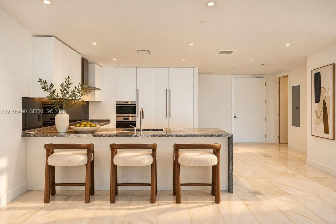 Modern kitchen featuring flat-panel cabinetry, stone countertops, integrated stainless steel appliances, recessed lighting, and large-format tile flooring