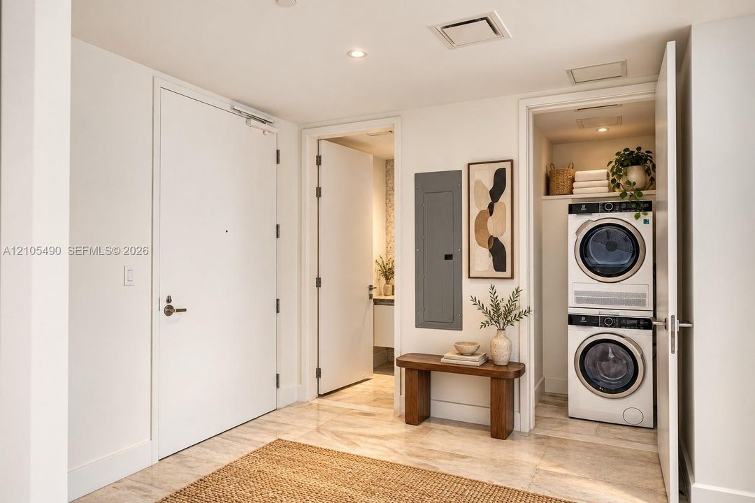 Neutral-toned stone flooring and recessed ceiling lighting throughout, featuring a dedicated laundry closet with a stacked washer and dryer, solid-core interior doors, and modern electrical panel