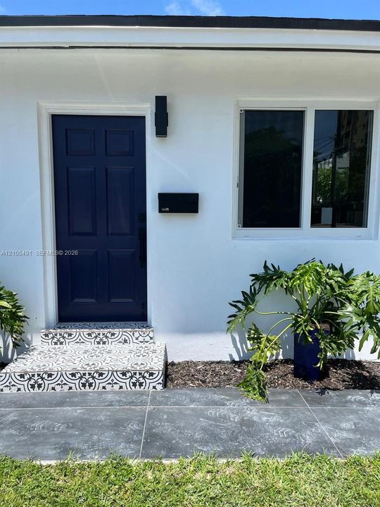 White exterior with contrasting navy paneled door, black wall-mounted light fixture, and patterned tile steps