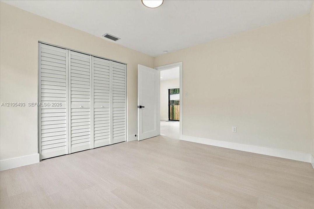 Interior space featuring light wood-finish flooring, neutral wall paint, white bi-fold louvered closet doors, and a shaker-style interior door with matte black hardware