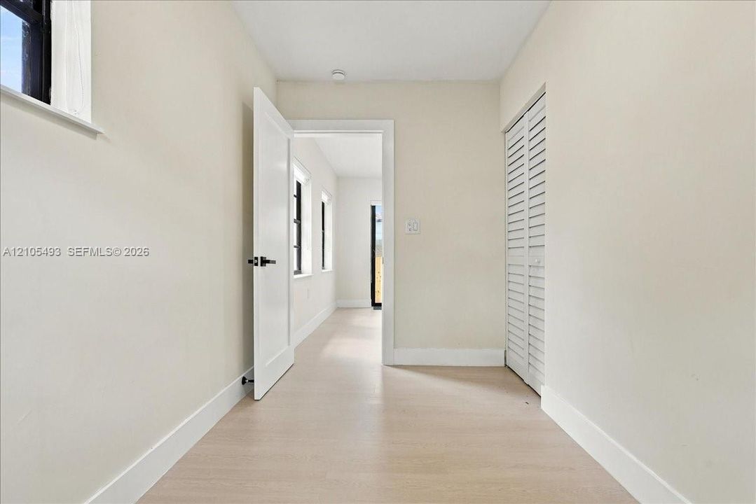 Interior space featuring neutral wall paint, wood-finish flooring, a white paneled door with matte black hardware, and white louvered closet doors