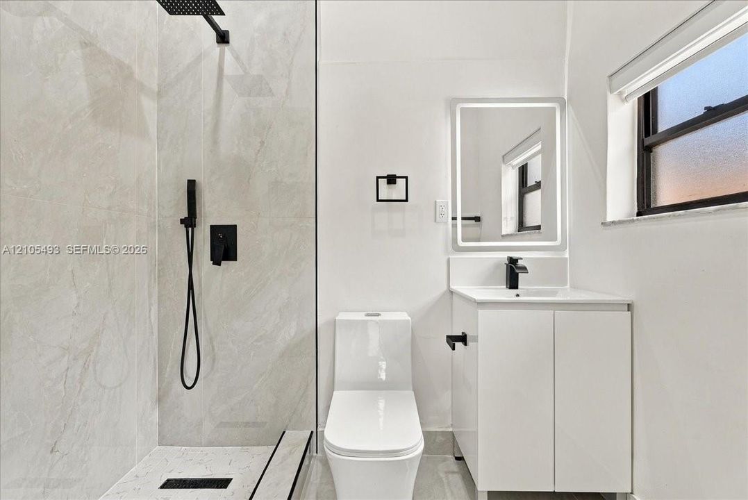 Bathroom featuring a glass-enclosed shower with matte black fixtures, rainfall showerhead, and floor-to-ceiling tile surround