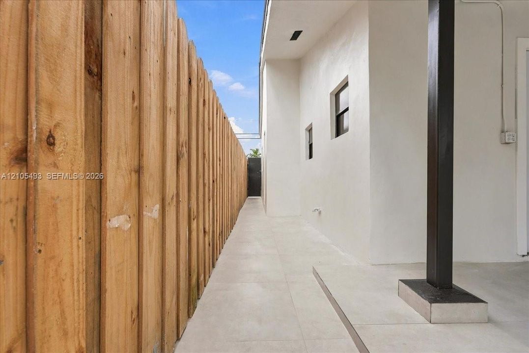 Exterior side passage featuring light-toned tile flooring, smooth stucco wall finish, and a full-height vertical wood privacy fence