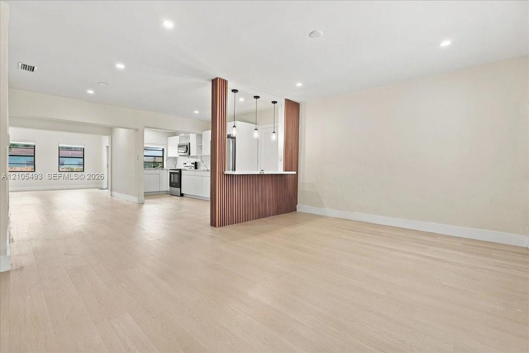 Open floor plan featuring wood-finish flooring, a wood-paneled peninsula with integrated counter seating, recessed lighting, and three pendant lights