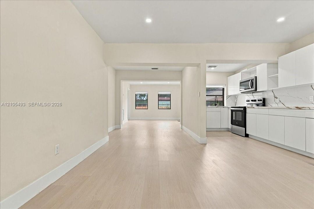 Kitchen featuring white cabinetry, stone-look countertops, stainless steel microwave, and wood-finish flooring throughout