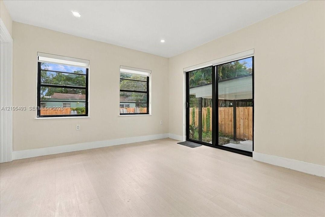 Interior space featuring light-toned wood-finish flooring, recessed lighting, neutral wall paint, multi-pane windows with black frames, and sliding glass doors