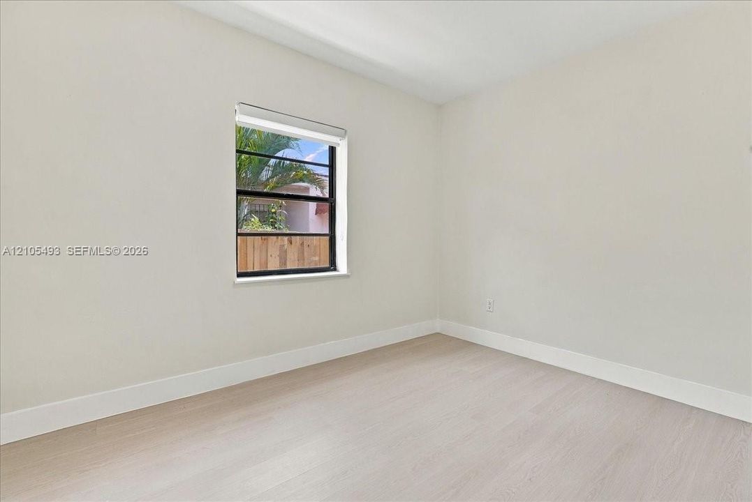 Neutral interior with light-toned wood-finish flooring, crisp white walls, and a single-pane window with black framing