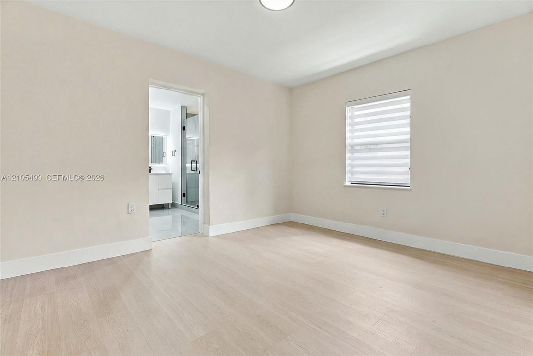 Neutral-toned interior space featuring light wood-finish flooring, a single-window configuration with horizontal blinds, and recessed ceiling lighting