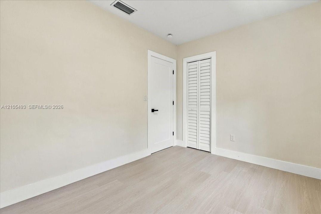 Neutral-toned interior space featuring light wood-finish flooring, a solid-panel door with matte black hardware, and a bifold closet door with louvered panels