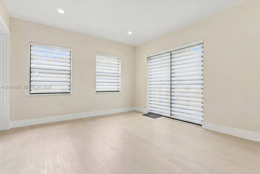 Neutral-toned interior featuring light-finished wood-style flooring, recessed lighting, and sliding glass doors with dual-layered roller shades