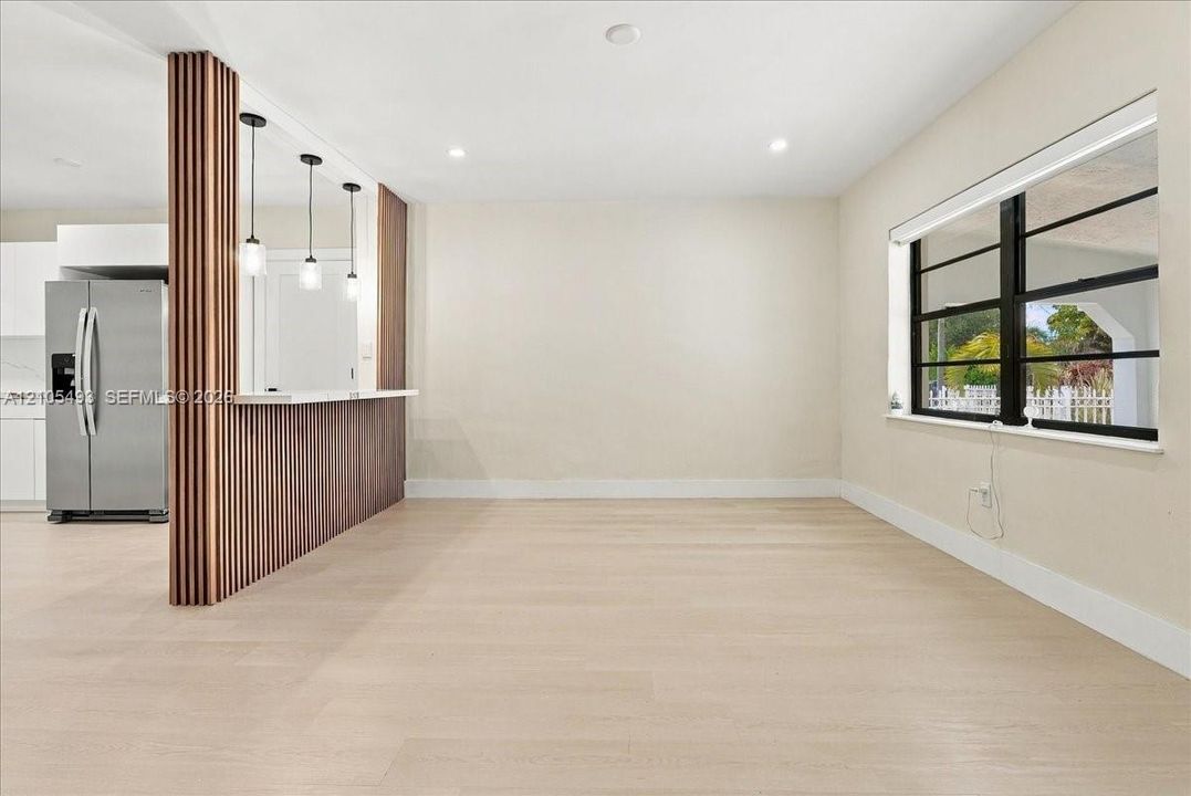Wood-finish flooring, custom vertical slat wood-finish partition wall, built-in breakfast bar with quartz countertop, pendant lighting, and horizontal multi-pane windows with black framing