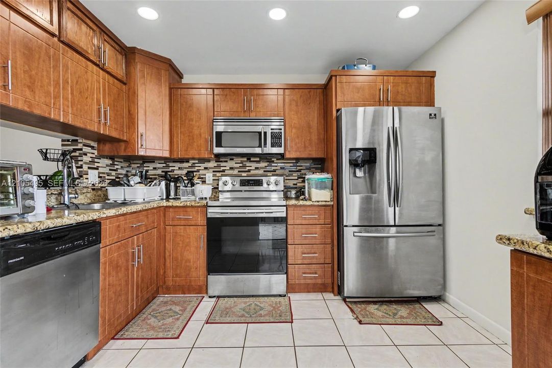 Kitchen featuring wood cabinetry, stone countertops, mosaic tile backsplash, recessed lighting, and stainless steel appliances
