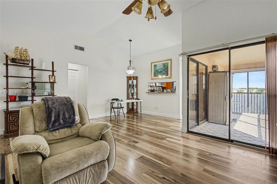 Open-concept area featuring vaulted ceilings, wood-finish flooring, a pass-through window to the kitchen, and sliding glass doors with water exposure