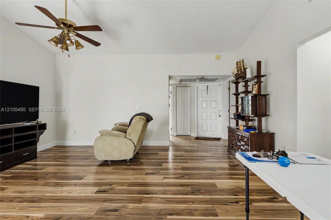 Wood-finish flooring, high ceilings, ceiling fan with multi-light fixture, and a six-panel entry door