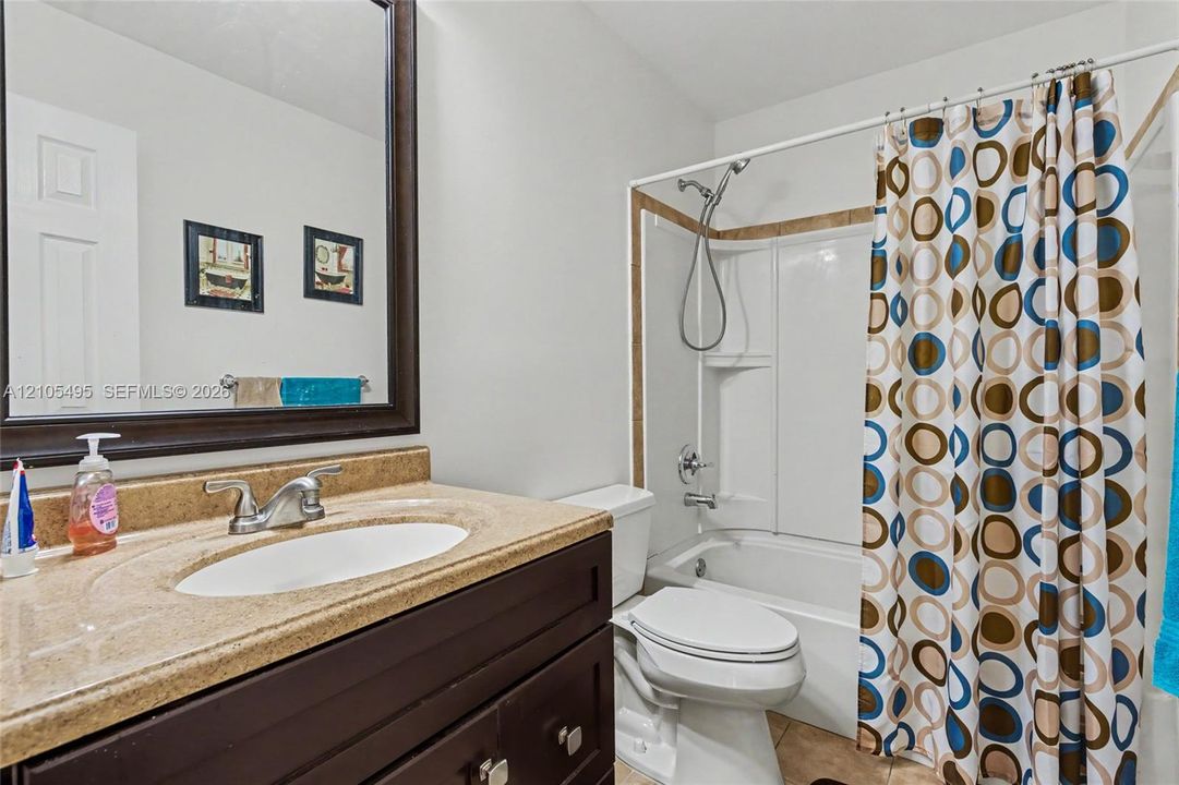Bathroom featuring a dark wood vanity with an integrated basin, a neutral-toned countertop, a large wall-mounted mirror with a matching dark frame, and a tub-shower combination with a detachable shower head
