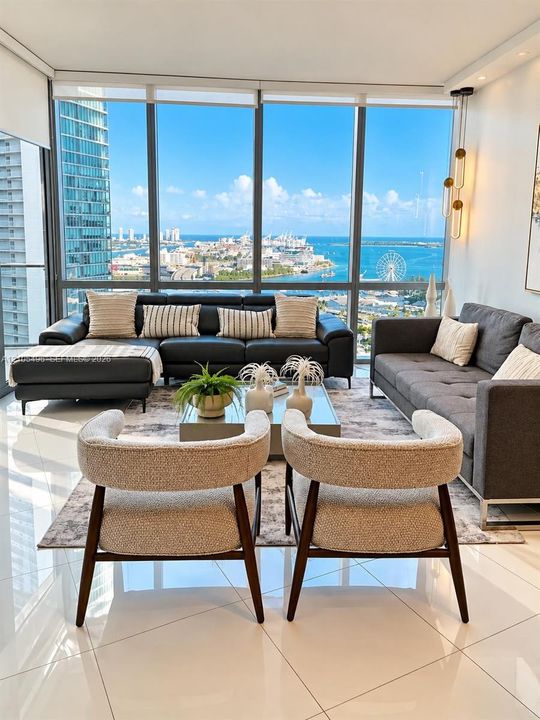 Floor-to-ceiling windows featuring panoramic water and city scenery, reflective polished tile flooring, and multi-light linear pendant lighting