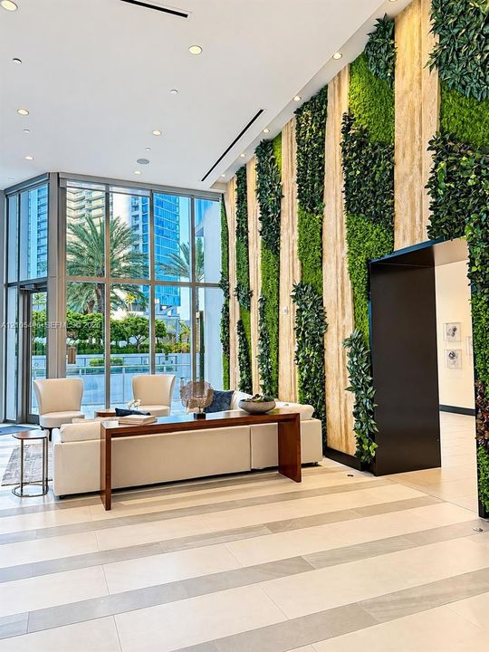 Floor-to-ceiling windows, vertical green plant wall, recessed lighting, and large-format tile flooring