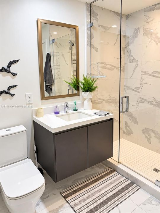 Wall-mounted vanity featuring a solid surface countertop, integrated sink, walk-in shower with floor-to-ceiling tile surround and glass enclosure, and white dual-flush toilet