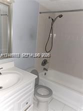 White vanity with integrated sink, white bathtub with shower fixture, and a toilet