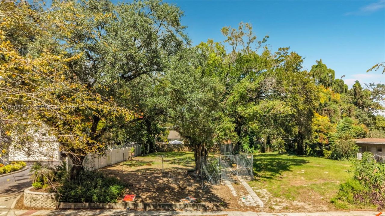 Level lot featuring mature trees, a chain-link perimeter fence, and concrete curbing