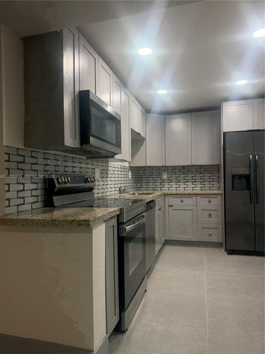 Kitchen featuring stainless steel appliances, light gray shaker cabinetry, stone countertops, and a subway tile backsplash